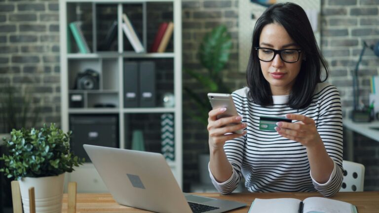 Woman shopping online with her phone and credit card at a laptop